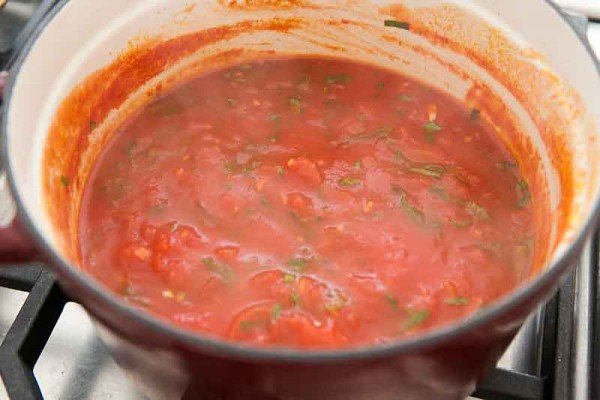 A dutch oven is on the stove with a marinara sauce cooking inside for easy eggplant parmesan.